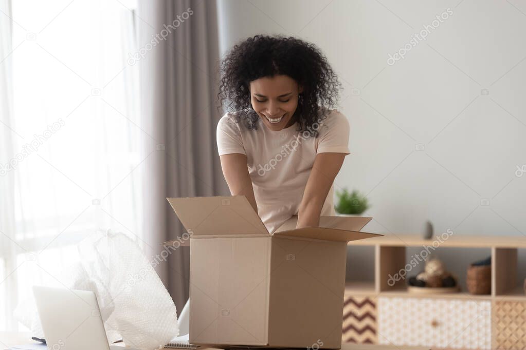 Smiling African American woman unpacking parcel, taking out goods