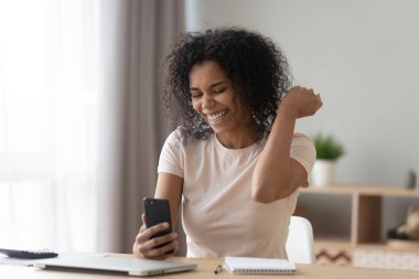 Mutlu Afrikalı Amerikalı kadın telefonu kullanarak başarıyı kutluyor.