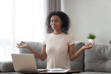 Tatmin olmuş Afro-Amerikan kadın dizüstü bilgisayar kullanıyor, evde meditasyon yapıyor.