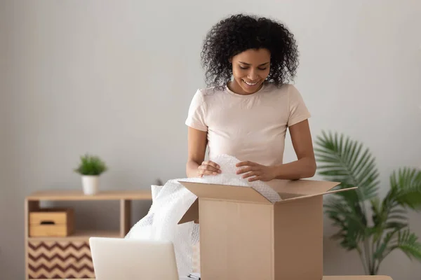 Lächelnde Afrikanerin packt Paket aus, entfernt Luftpolsterfolie — Stockfoto