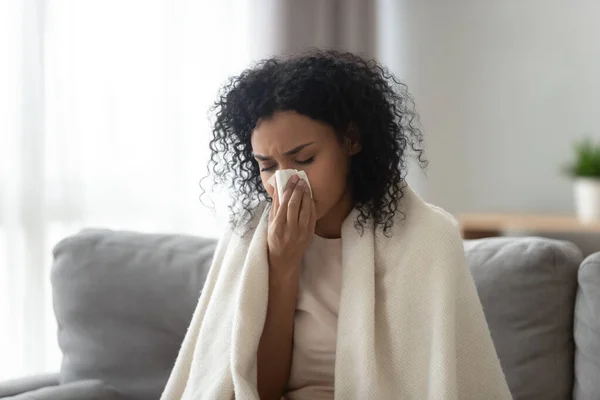 Sick African American woman covered blanket blowing nose