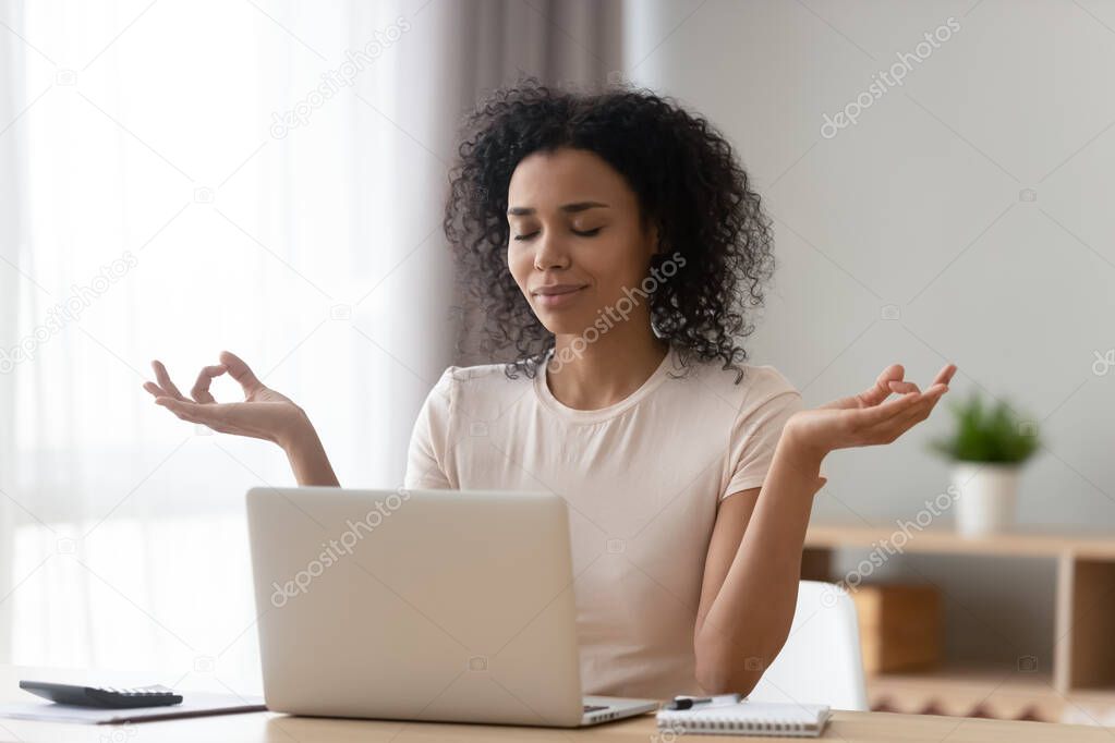 Calm African American woman meditating at desk with laptop