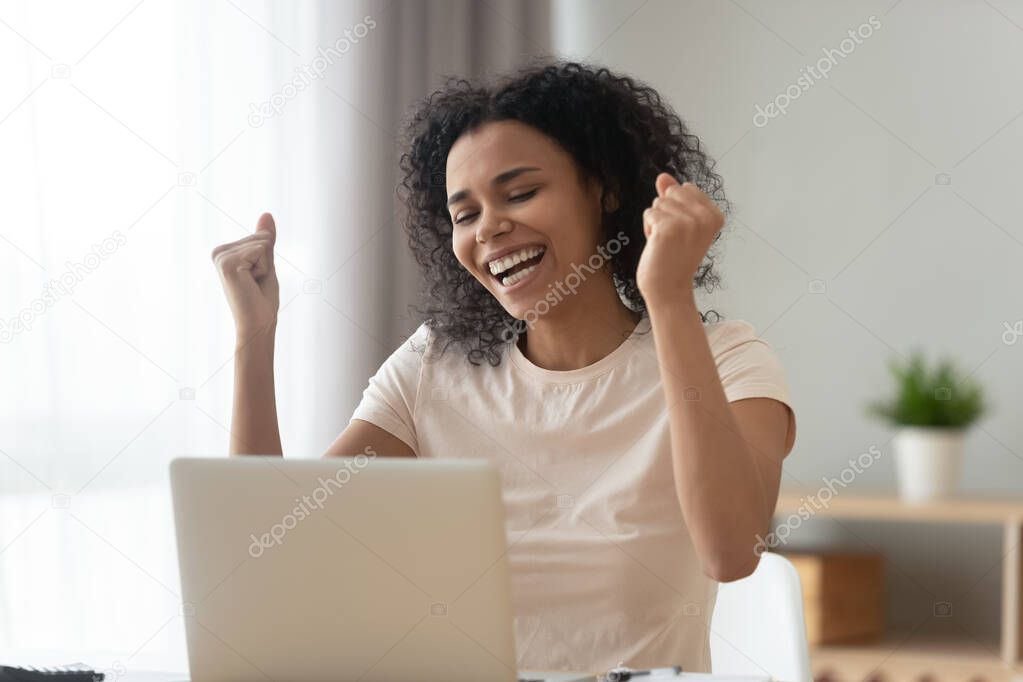 Overjoyed African American woman excited by online success, using laptop