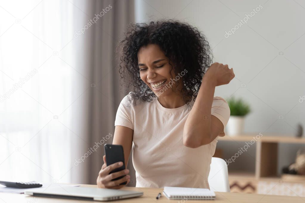 Happy African American woman using phone, celebrating success