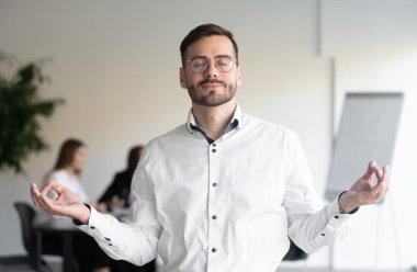 Sakin bir iş adamı ofiste gözleri kapalı meditasyon yapıyor.