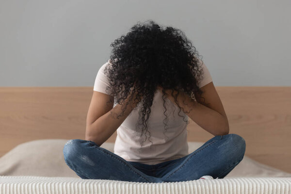 Unhappy African American woman sitting alone in bed, feeling lonely