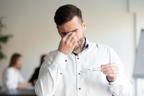 Tired male employee take off glasses suffering from headache — Stock Photo, Image