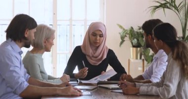 Asyalı Müslüman kadın şirket lideri takım toplantısında evrak işlerini tartışıyor.