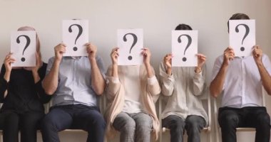 İşsizler kuyrukta oturup sorularla yüzlerini gizlerler.