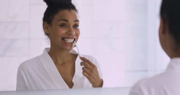 Happy healthy young african woman brushing teeth looking in mirror — Stock Video