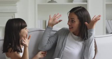 Küçük bir kız çocuğu kanepeyi gıdıklayarak mutlu annesiyle oynuyor.