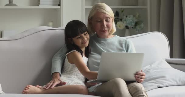笑顔成熟した祖母と孫娘笑います使用してノートパソコン上のソファ — ストック動画