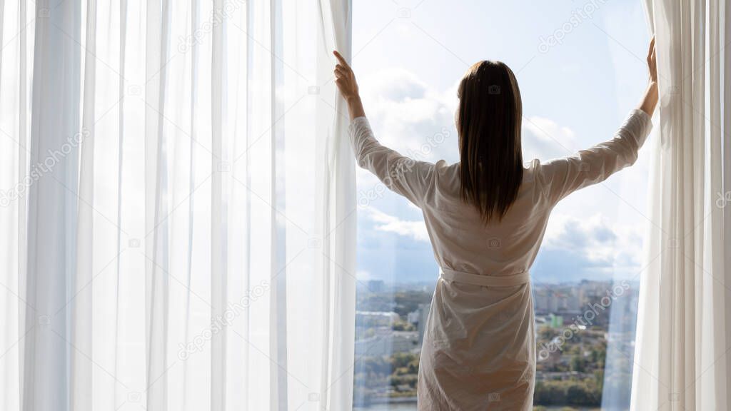 Rich young woman wear gown open curtains stand at window