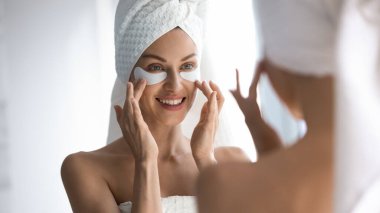 Happy woman towel on head apply patches looking in mirror clipart