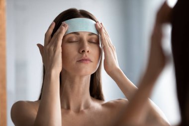 Genç ve çekici bir kadın alnına bant yapıştırıyor. Yüzündeki kırışıklıkları düzeltiyor.