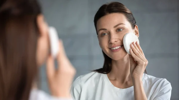 Sorrindo bela senhora limpeza purificando a pele facial segurando esponja esfoliante — Fotografia de Stock