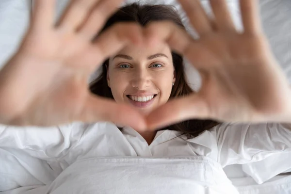 Gelukkig jong vrouw tonen hart met handen liggend in bed — Stockfoto