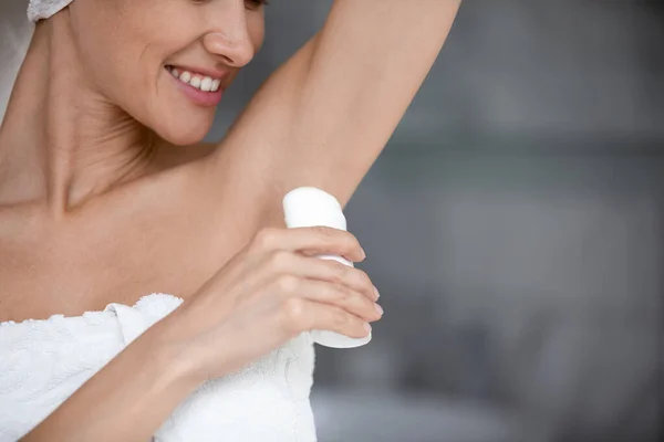 Smiling woman wrapped with towel applying antiperspirant stick in armpit — Stock Photo, Image