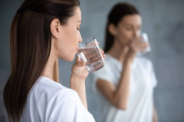 Woman holding glass drinking water in morning reflecting in mirror — Stock Photo, Image