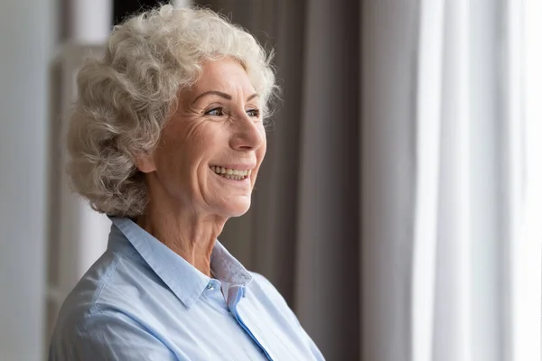 Szczęśliwa starsza kobieta spogląda przez okno marząc o nadziei — Zdjęcie stockowe