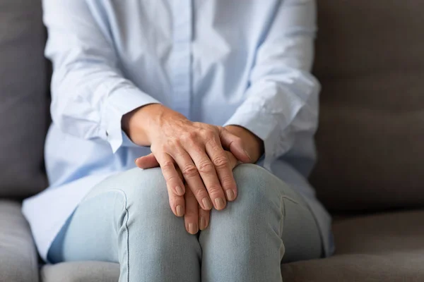 Senior mulher solitária sentar no sofá com as mãos dobradas, close-up — Fotografia de Stock