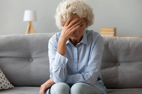 Depressive alte Frau sitzt auf Sofa und leidet unter Kopfschmerzen — Stockfoto