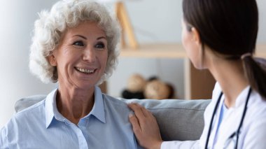 Yaşlı hastaya yardım eden genç hemşireye bakan mutlu büyükanne.