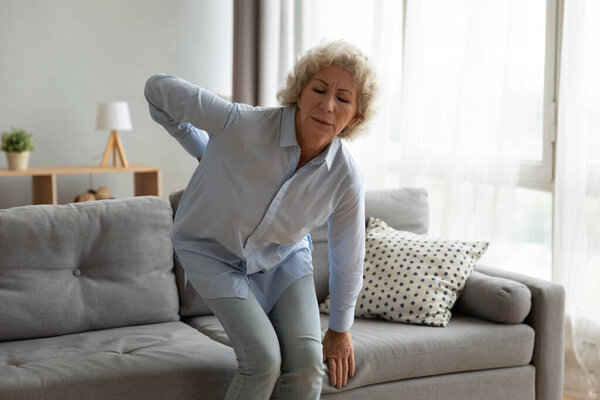 Old lady touching back feel ache getting up from sofa