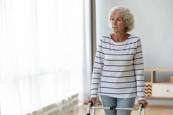Przemyślana, smutna, zraniona staruszka stojąca samotnie używając chodzącej ramy — Zdjęcie stockowe