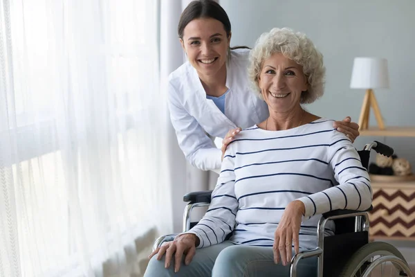 Happy disabled grandma on wheelchair and nurse look at camera — Stock Photo, Image