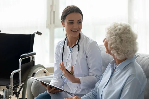Mutlu genç kadın doktor engelli yaşlı büyükanne hastaya danışıyor. — Stok fotoğraf