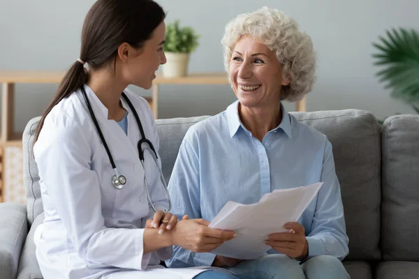 Mujer joven médico consultar feliz anciana abuela paciente celebrar papeles —  Fotos de Stock