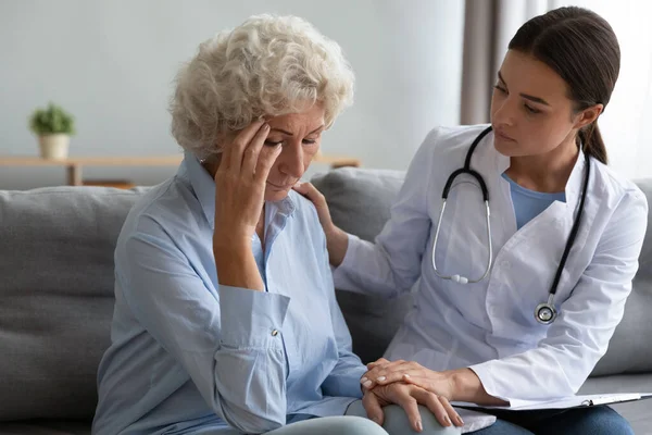 Young female nurse doctor comforting consoling sad old grandmother patient — Stock Photo, Image