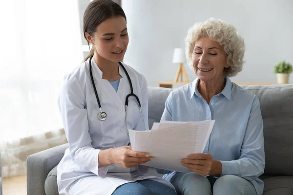 Mujer mayor sonriente paciente y médico joven leyendo contrato de seguro — Foto de Stock