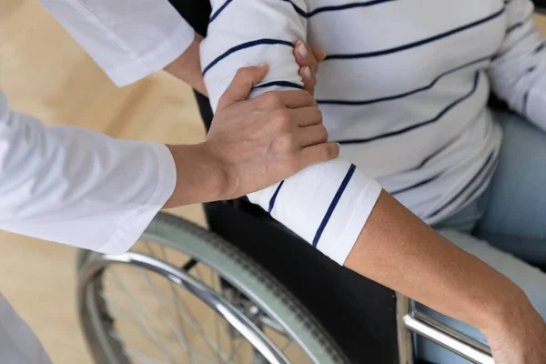 Ajudando a mão do zelador segurando mulher idosa na cadeira de rodas, close-up — Fotografia de Stock