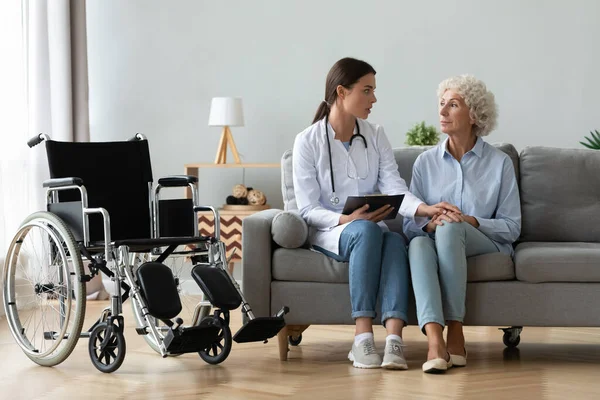 Allvarlig kvinnlig läkare tröstar skadade funktionshindrade äldre dam patient — Stockfoto