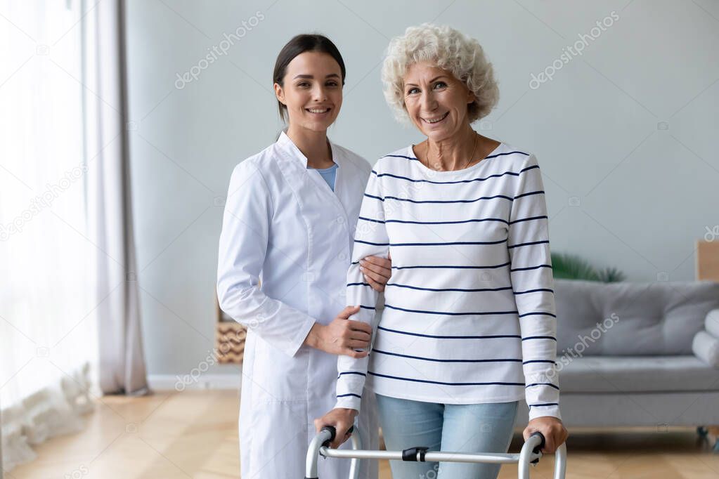 Female physiotherapist help old woman using walker look at camera