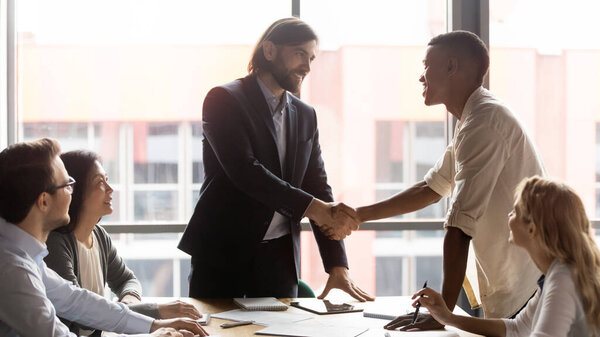 Улыбающийся лидер команды пожимает руку счастливому африканскому сотруднику из Америки
.