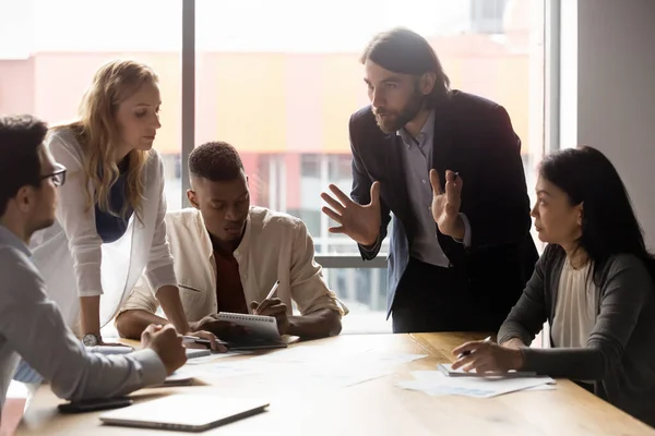 Joven empresario serio inclinándose sobre la mesa, explicando ideas a sus compañeros de equipo . — Foto de Stock