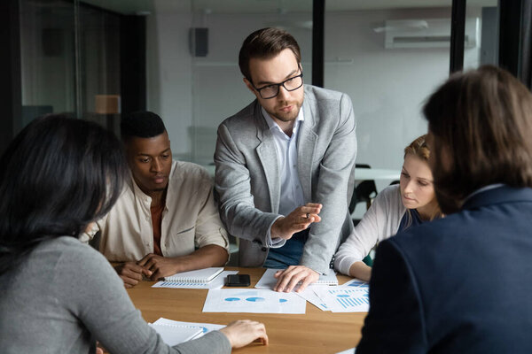 Focused confident young employee sharing ideas with focused group.