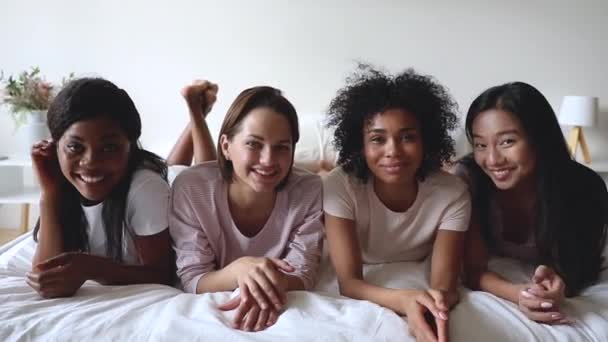Multiraciala kvinnor vänner bär pyjamas tittar på kameran på sängen — Stockvideo
