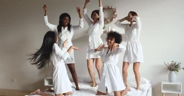Boldog változatos lányok barátok viselnek köntöst tánc az ágyban — Stock videók