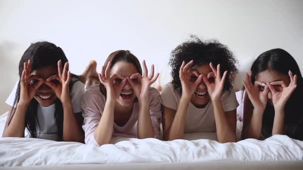 Cheerful funny multiethnic girls having fun make binoculars on bed — Stock Video