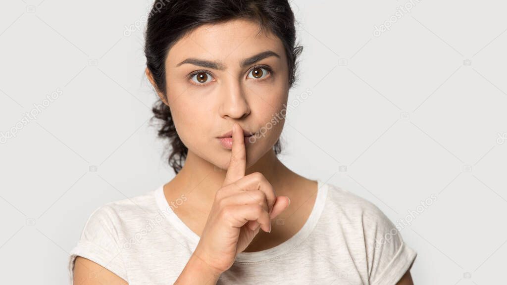 Headshot portrait serious Indian woman showing hush gesture close up