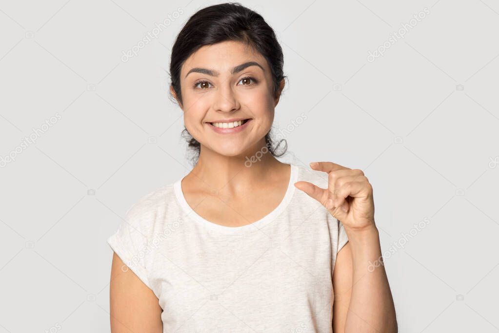 Smiling satisfied Indian girl showing little size gesture with fingers