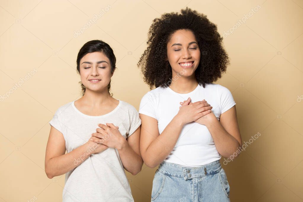 Smiling grateful diverse girls holding hands on chest