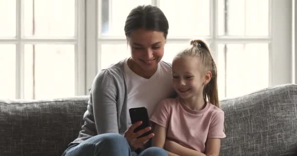 Happy mam en kind dochter genieten met behulp van smartphone op de bank — Stockvideo