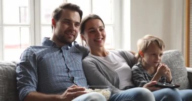 Mutlu aile babaları ve küçük oğlu birlikte televizyon izlerken gülüyorlar.