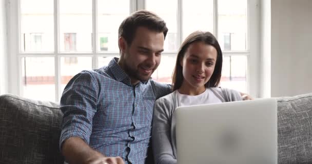 Счастливая молодая пара разговаривает связи с помощью ноутбука сидеть на диване — стоковое видео