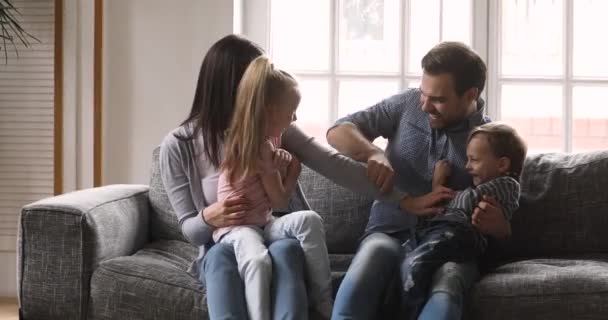 Padres felices juguetones y niños pequeños jugando cosquillas en el sofá — Vídeos de Stock